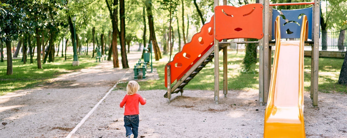 Ein kleines Kind läuft über einen Spielplatz zu einer Rutsche.
