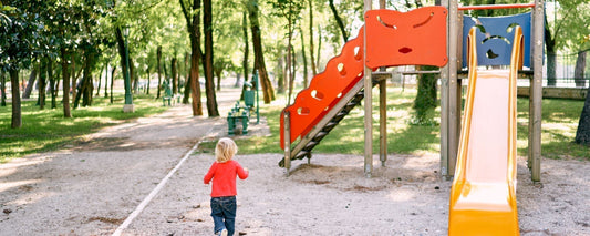 Ein kleines Kind läuft über einen Spielplatz zu einer Rutsche.
