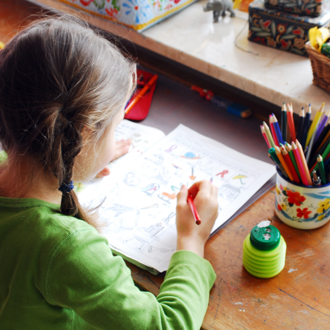 Mädchen sitzt am Schreibtisch und malt Bilder aus.