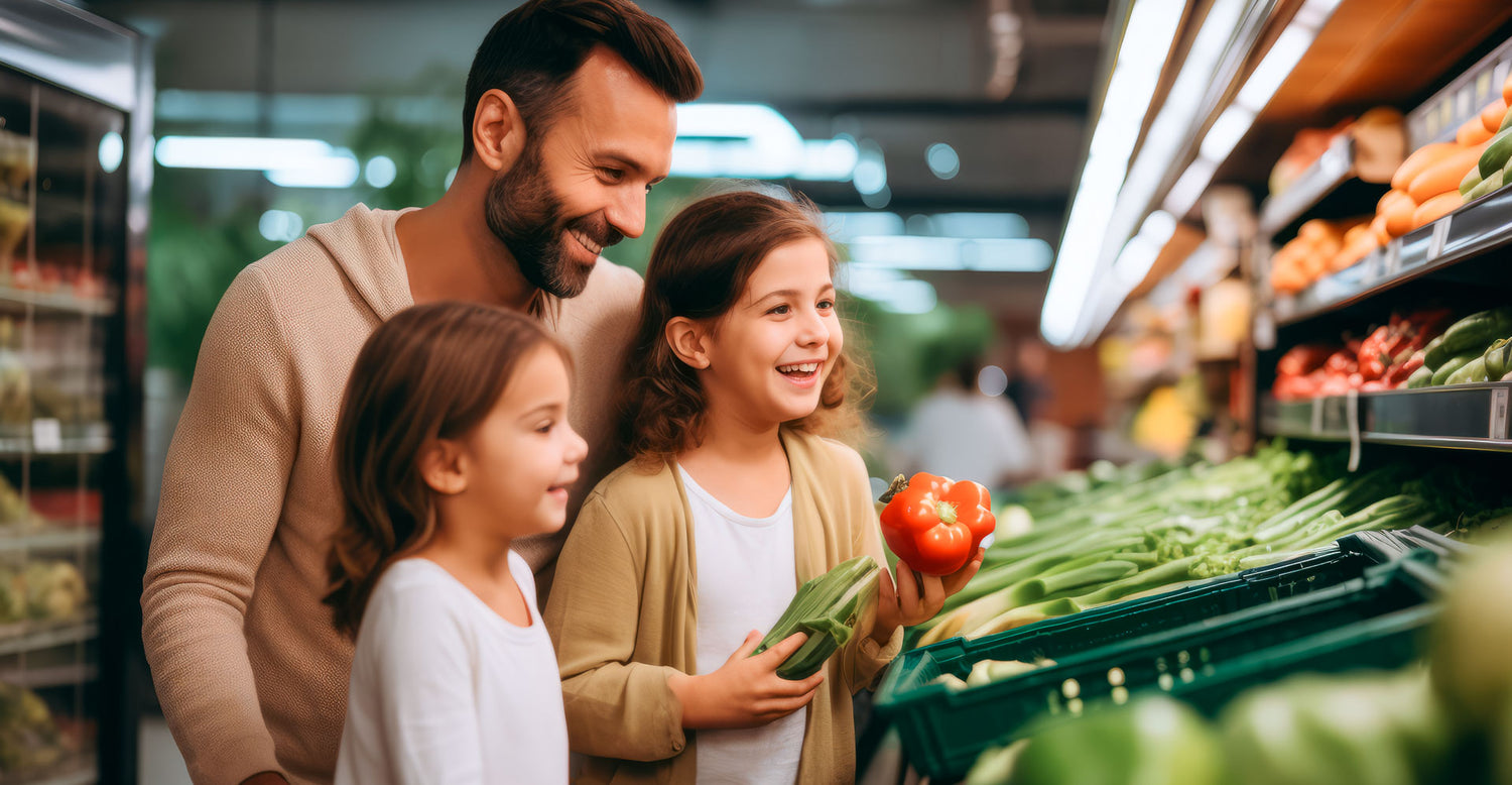 Vater mit zwei Kindern im Supermarkt beim Gemüseregal