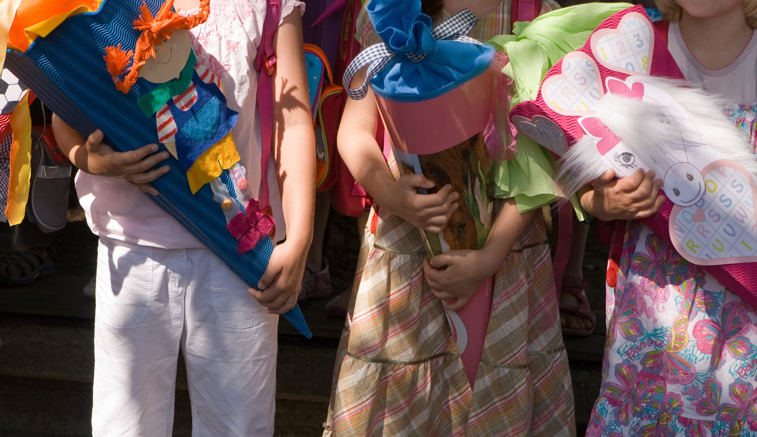 Drei Kinder halten ihre bunten Schultüten am 1. Schultag