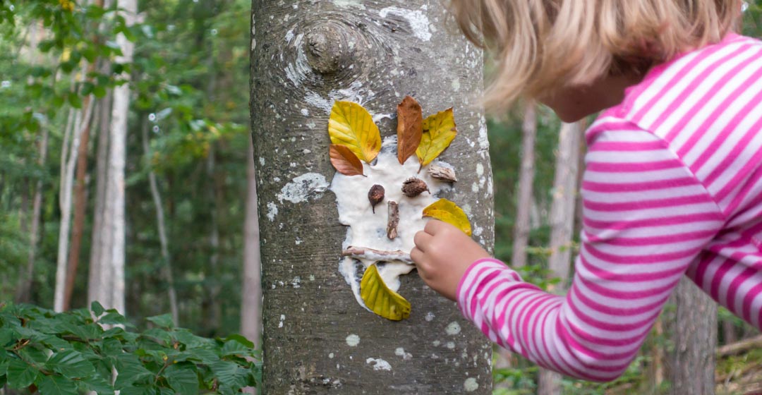 Kind kreiert Gesicht auf Baumrinde mit Blättern und weißem Mehl-Wasser-Kleber