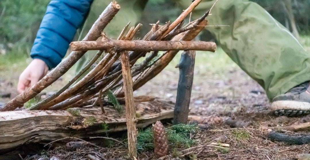 Kind baut Wichtelaus aus Zweigen, Steinen, Blaettern und Zapfen