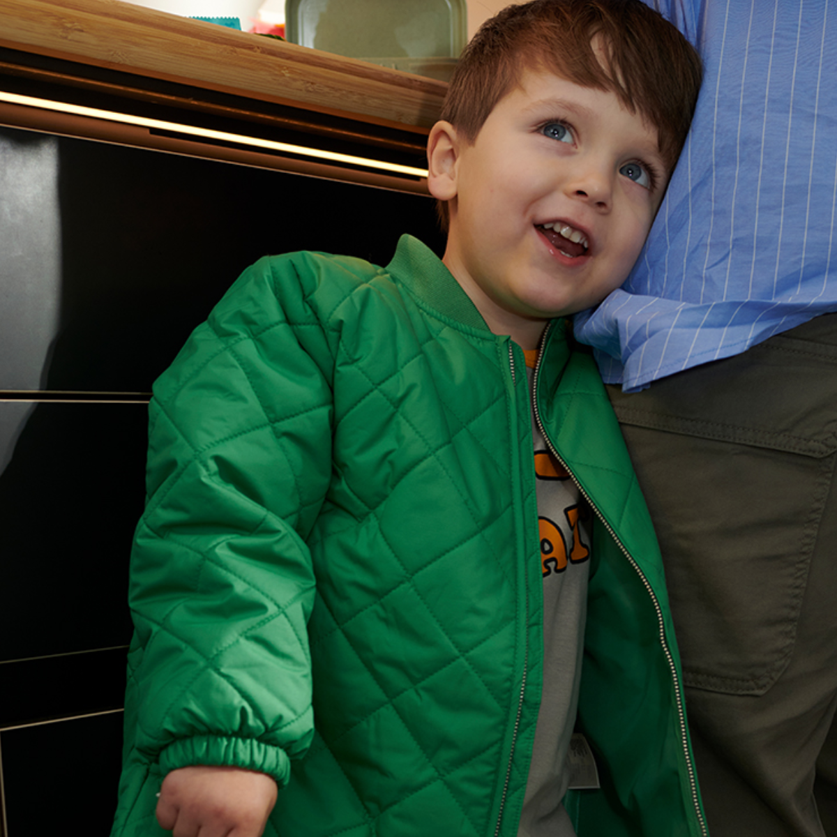 Kind steht neben einem Elternteil in der Küchen und schaut nach oben.