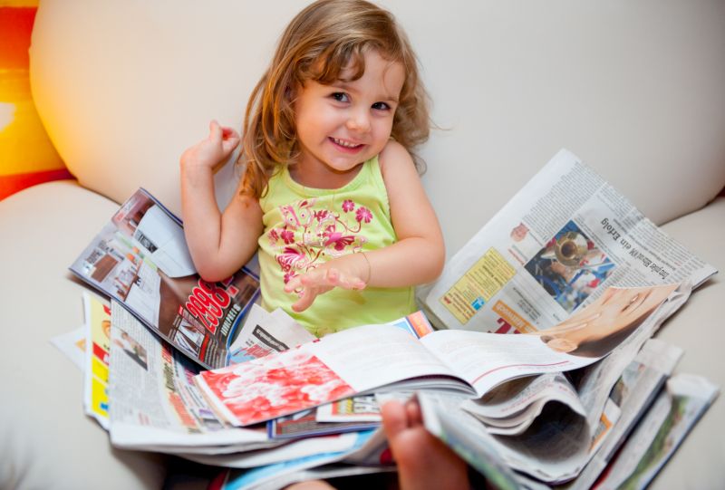 Kind sitzt, offene Print-Zeitung auf Schoss