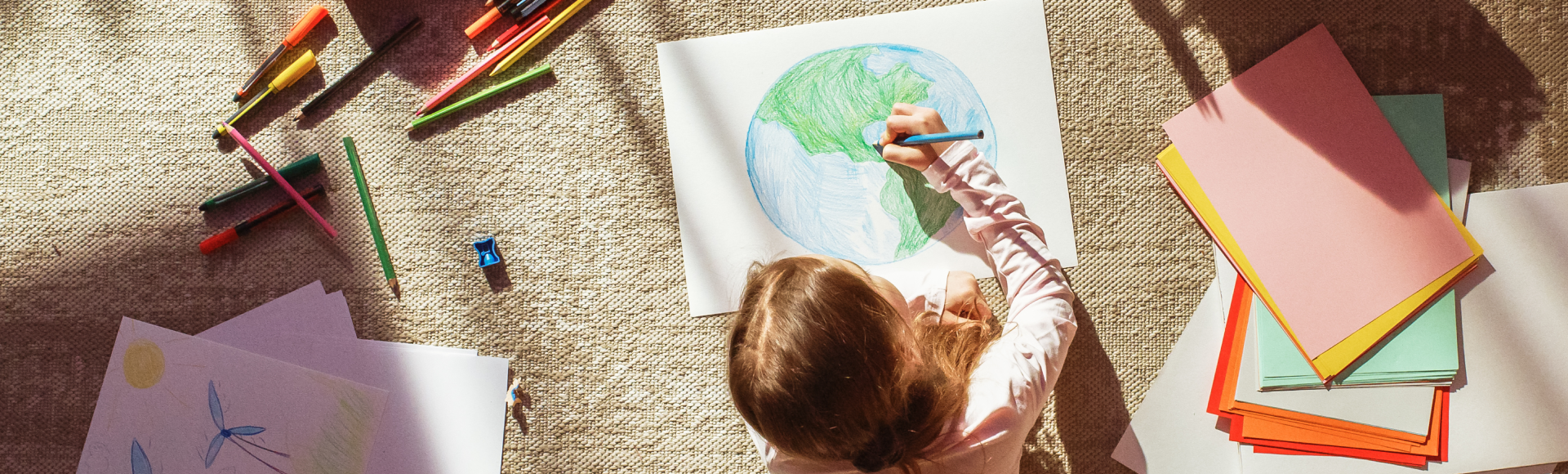 Mädchen, das auf dem Boden liegt und eine Weltkugel auf einem weißen Papier malt.